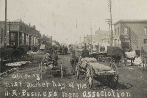 black and white photograph of horse-drawn wagons on a busy dirt road